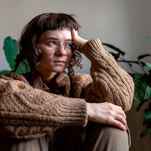 Una persona joven de piel clara con cabello castaño corto y flequillo, y gafas redondas, parece pensativa o preocupada.